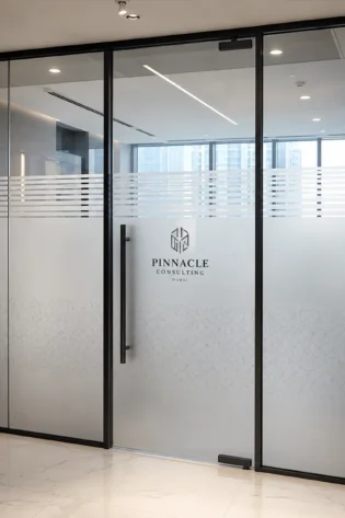 Frosted glass office partition with geometric pattern and Pinnacle Consulting Dubai logo.