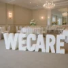 Large freestanding white 3D letters spelling “WECARE” displayed in an elegant indoor event venue.
