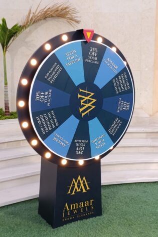 LED spin the prize wheel with Amaar Jewels branding placed at an outdoor venue, featuring illuminated lights, promotional prize segments, and a sturdy display stand for events and activations.